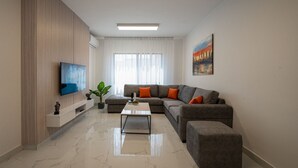 A modern living room with a sectional sofa, a flat-screen TV, a coffee table, and a painting on the wall.
