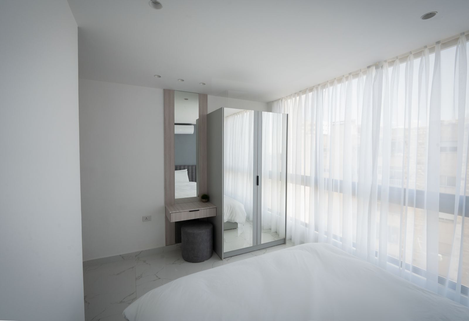 Une chambre d’hôtel moderne avec un grand lit, un miroir, une petite table et une poubelle.