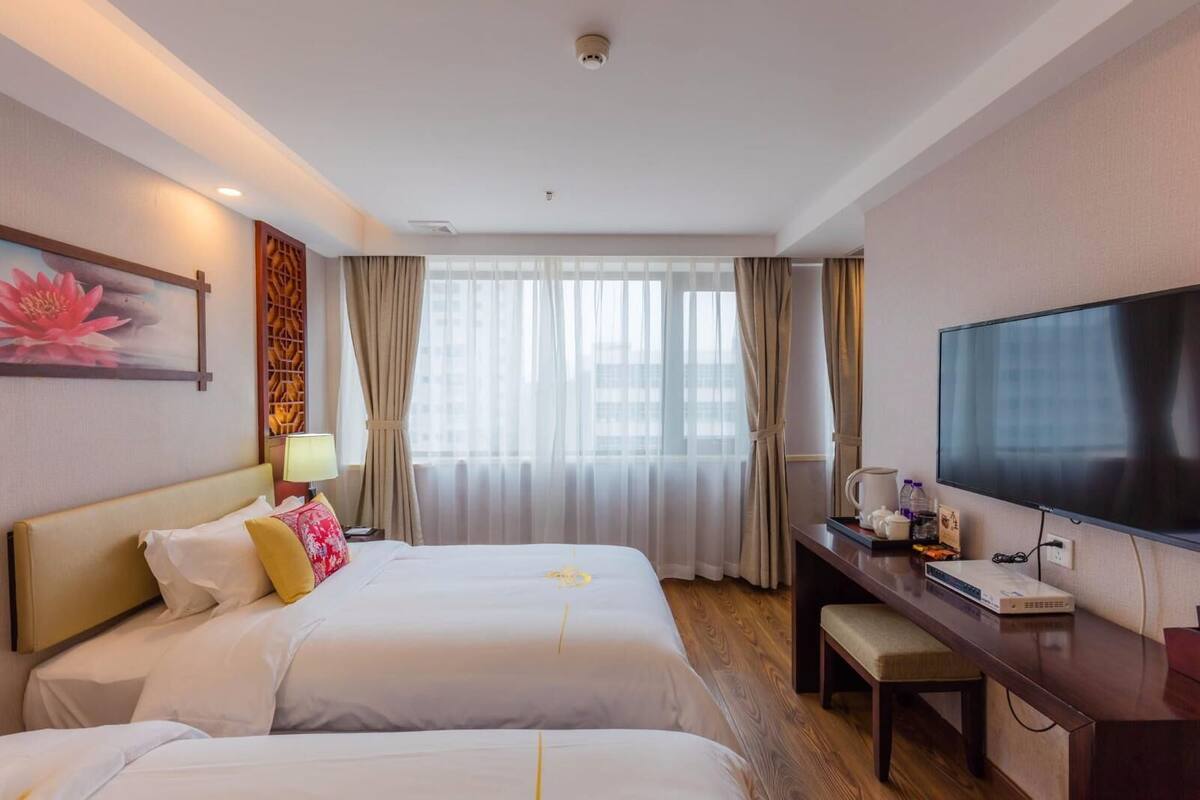 A hotel room with two beds, a desk, a television, and a window with curtains.