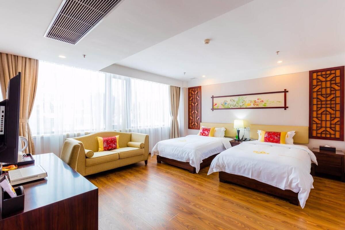 A hotel room with two beds, a desk, a sofa, and a TV.