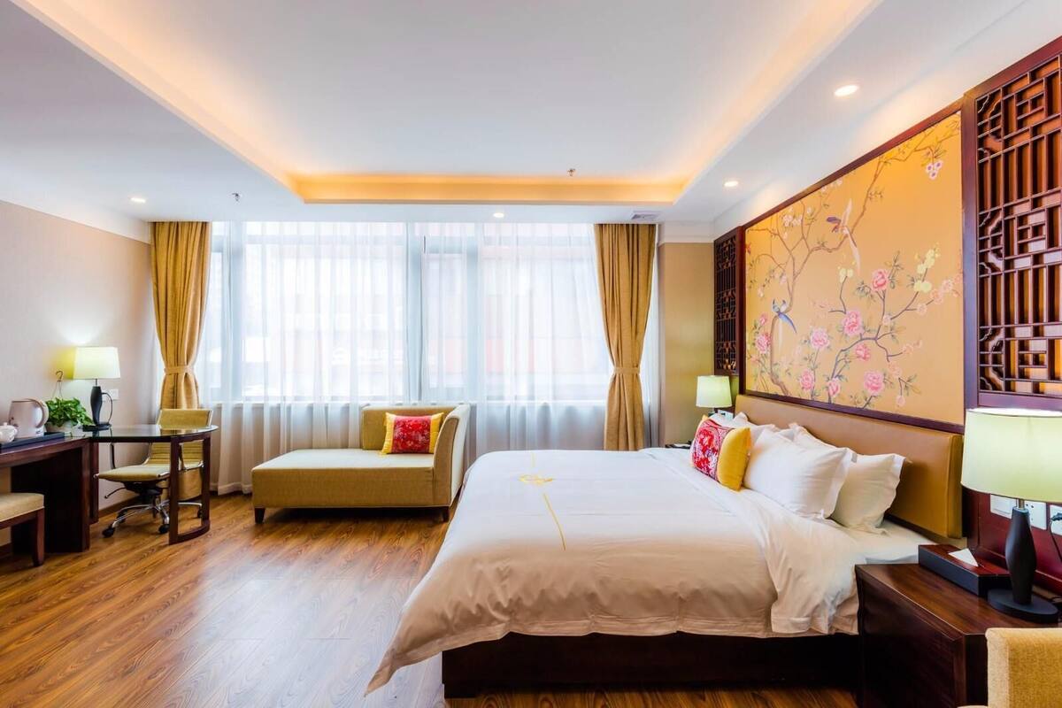 A hotel room with a bed, a desk, a sofa, and a large window with curtains.