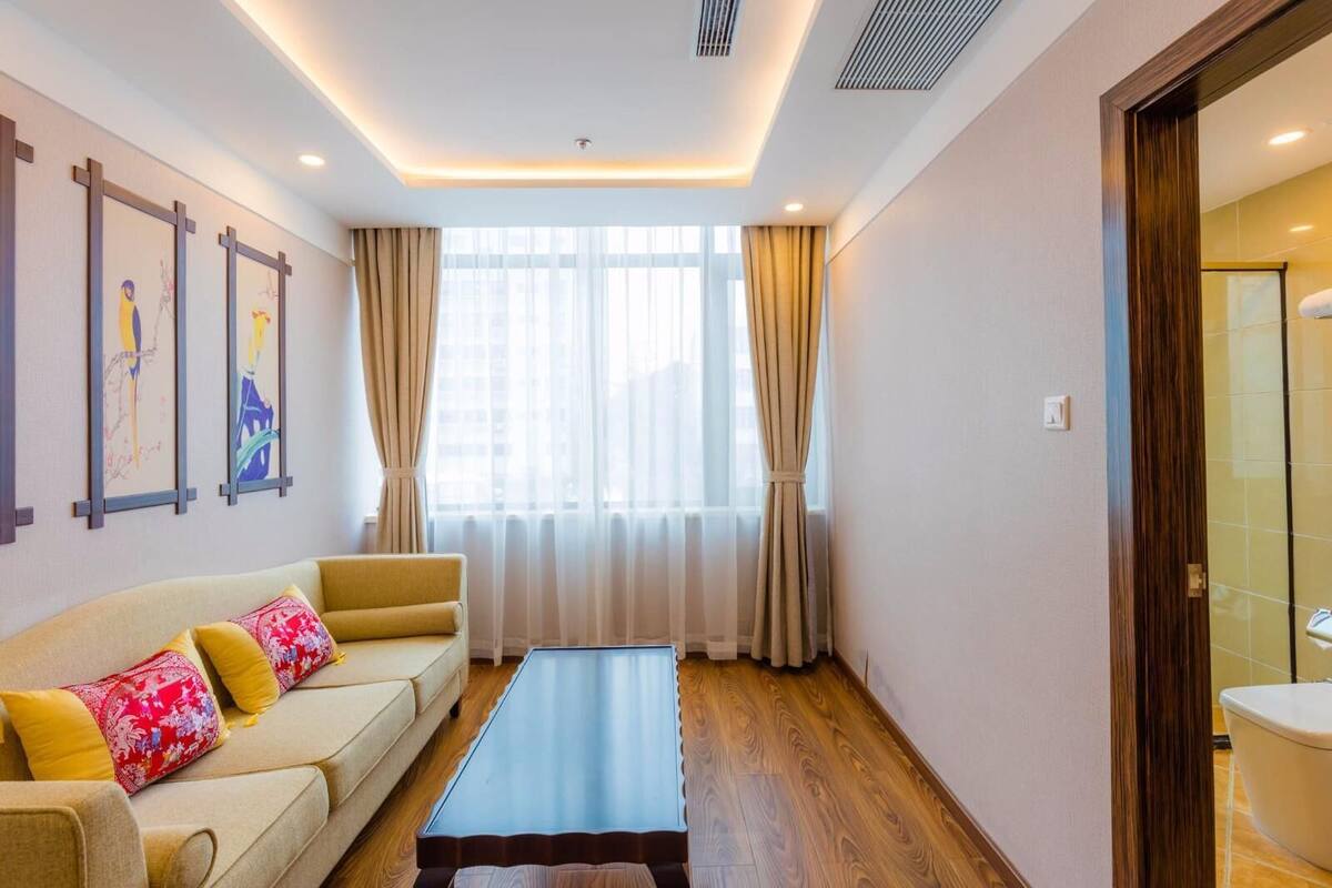 A modern living room with a sofa, a coffee table, and a large window with curtains.