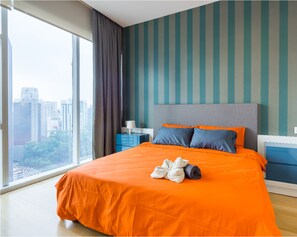 A modern hotel room with a large bed, a view of the city, and a striped wall. - BedStay Platinum Suites (Kuala Lumpur)