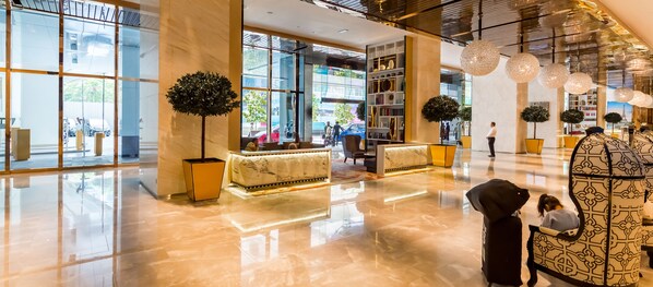 Un vestíbulo amplio con suelo de mármol, ventanas grandes y una mesa de recepción.