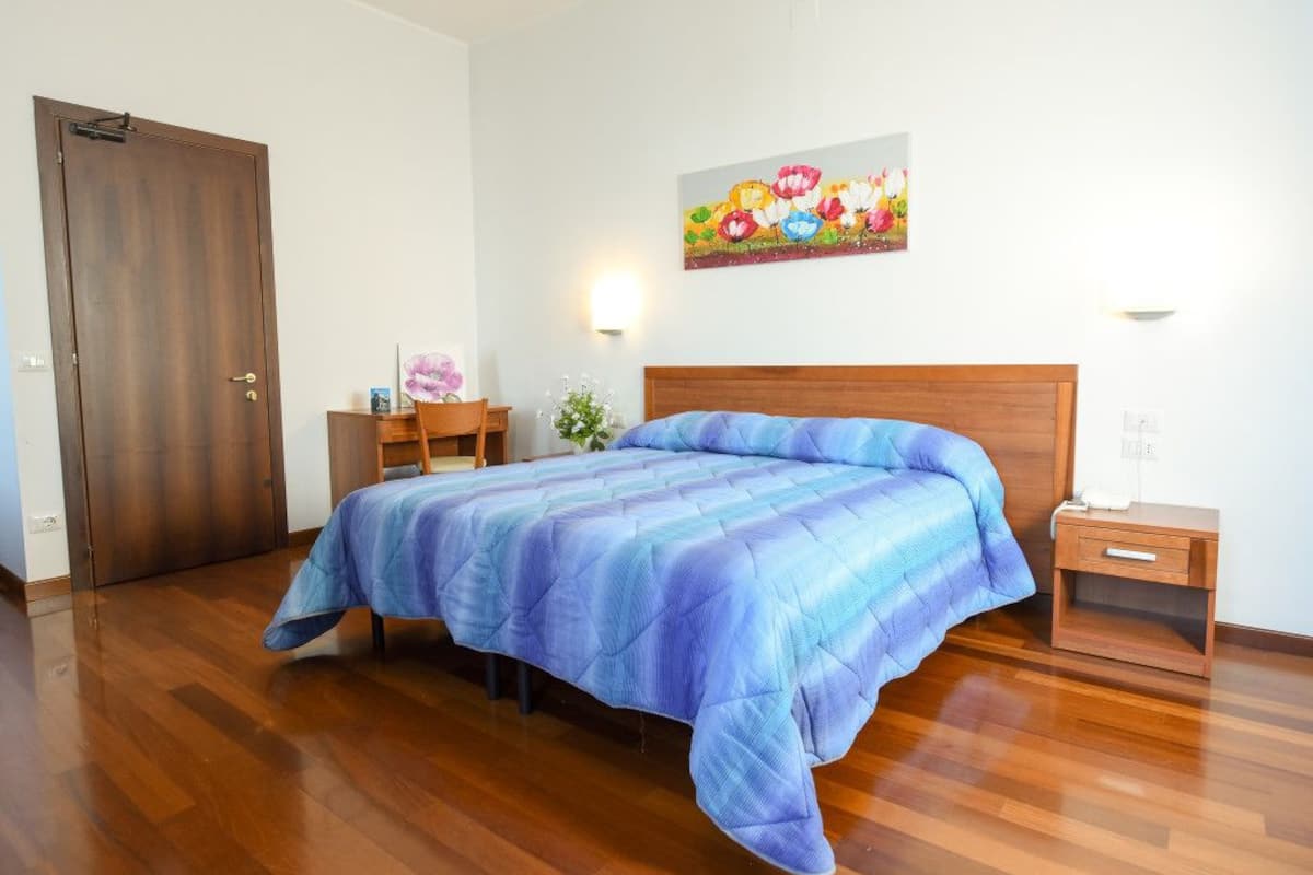 A bedroom with a wooden bed, a nightstand, a chair, and a door.