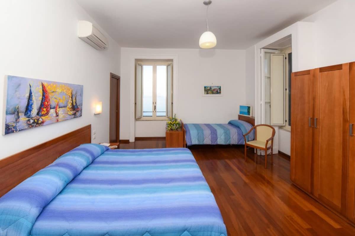 A room with two beds, wooden wardrobe, and a painting on the wall.