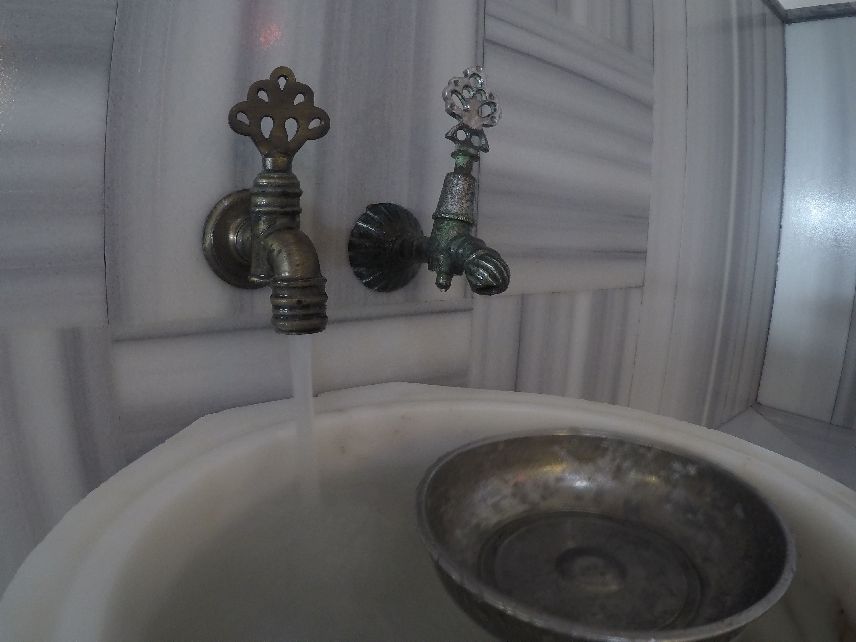 Un baño con un lavamanos blanco, dos grifos y una pileta de metal.