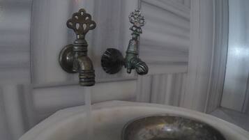Un baño con un lavamanos blanco, dos grifos y una pileta de metal.
