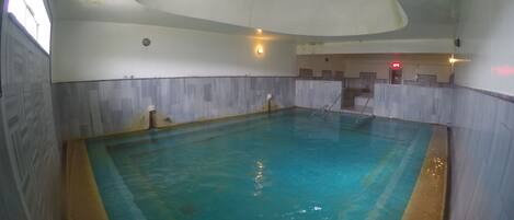En inomhuspool med kaklade golv och väggar, ett välvt tak med infälld belysning och en tydligt synlig utrymningsskylt.