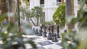 Un tablero de ajedrez dispuesto al aire libre, con un edificio al fondo.