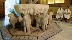 Interior de un edificio histórico con una gran y ornamentada fuente, detalles en piedra labrada y piso de baldosas.