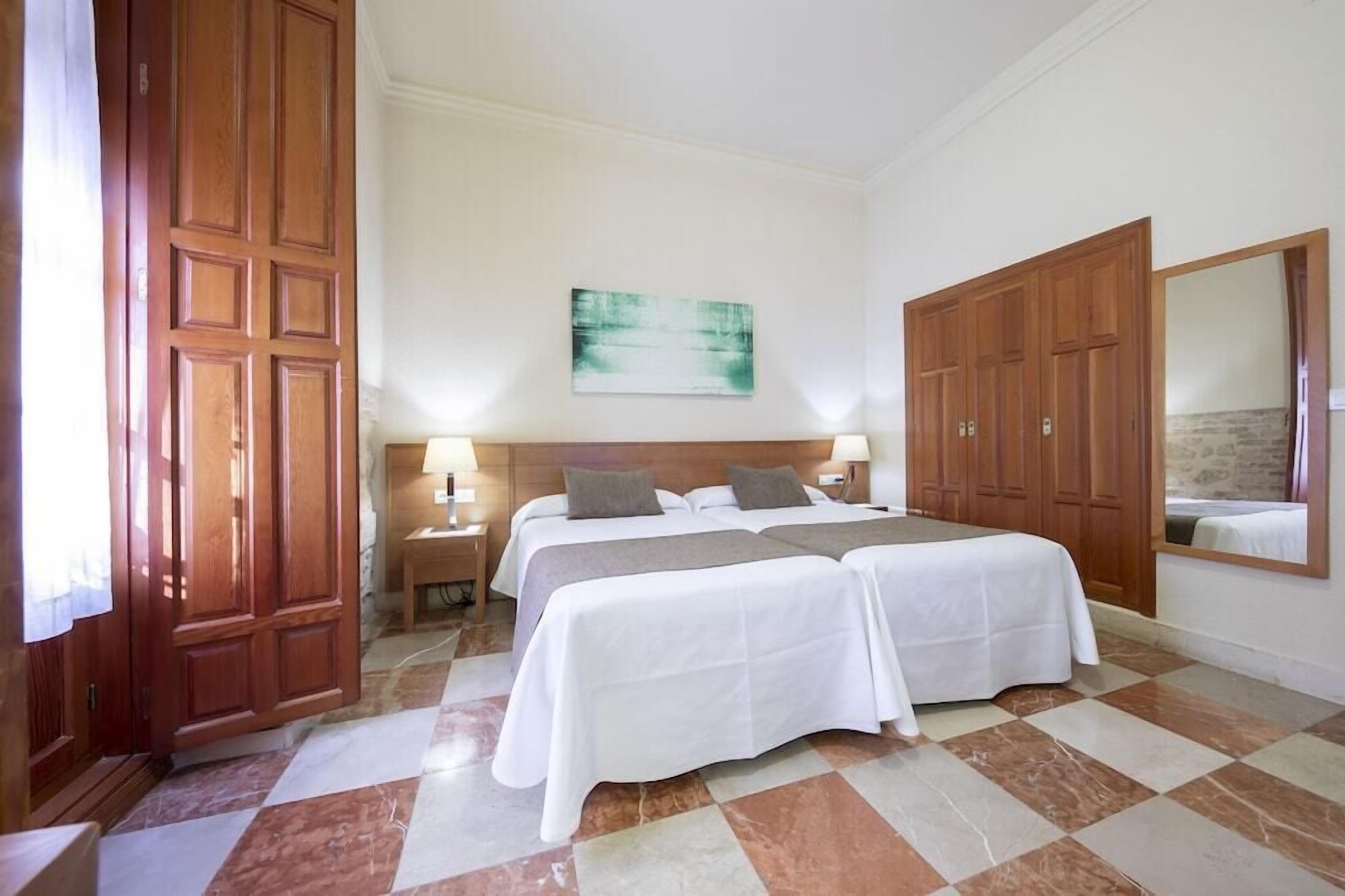 A hotel room with two beds, a large mirror, and a painting on the wall.