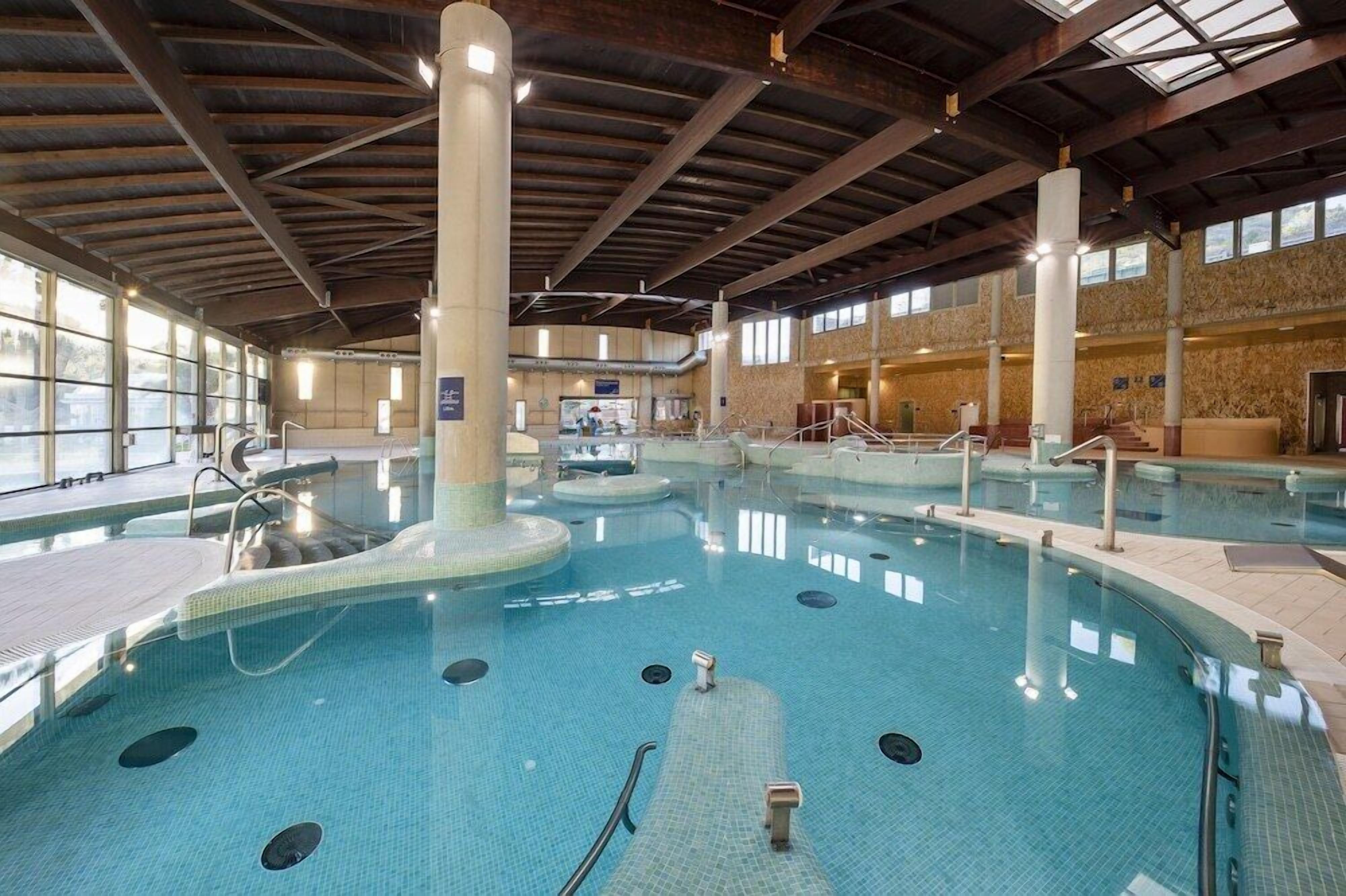 Een binnenzwembad met helder water, meerdere banen en een centrale pilaar.