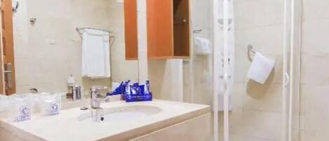 Un baño con lavamanos, espejo y ducha con mampara de vidrio.