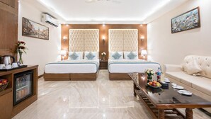 A hotel room with two beds, a sofa, a coffee table, a TV, and a minibar. - OPO Viva Palace (New Delhi)