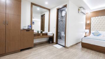 Habitación de hotel con un armario de madera, un espejo, una mesita de noche con lámpara y una cama con cabecero capitonado.