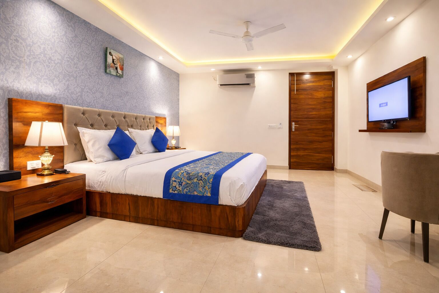 A hotel room with a bed, nightstand, lamp, TV, and a ceiling fan.