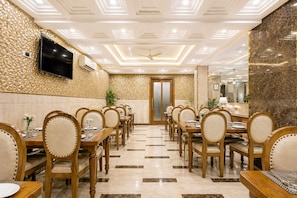 A hotel dining area with wooden tables and chairs, a flat-screen TV, and a ceiling fan. - OPO Viva Palace (New Delhi)