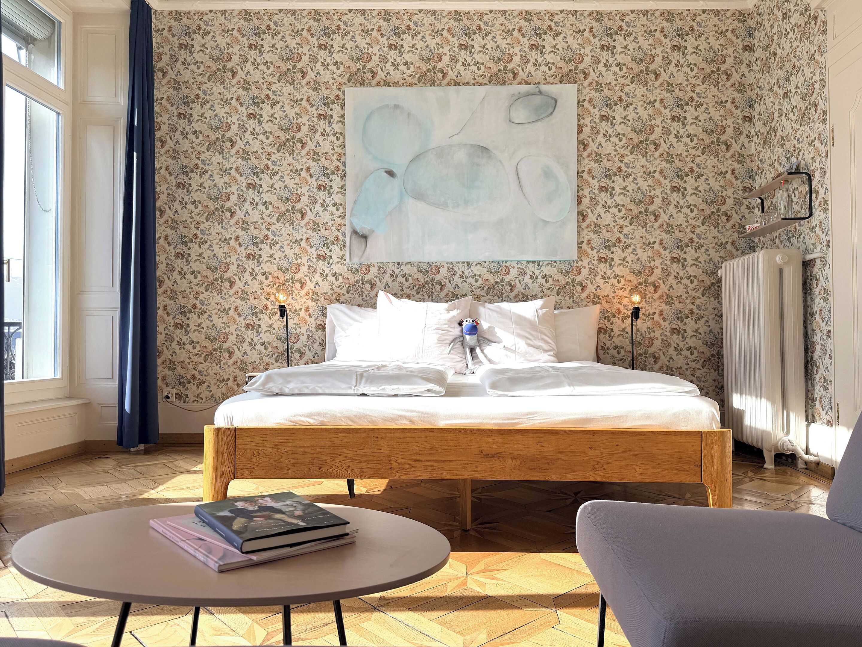Un dormitorio con cama, dos lámparas de noche, una mesa redonda con un libro y una silla.