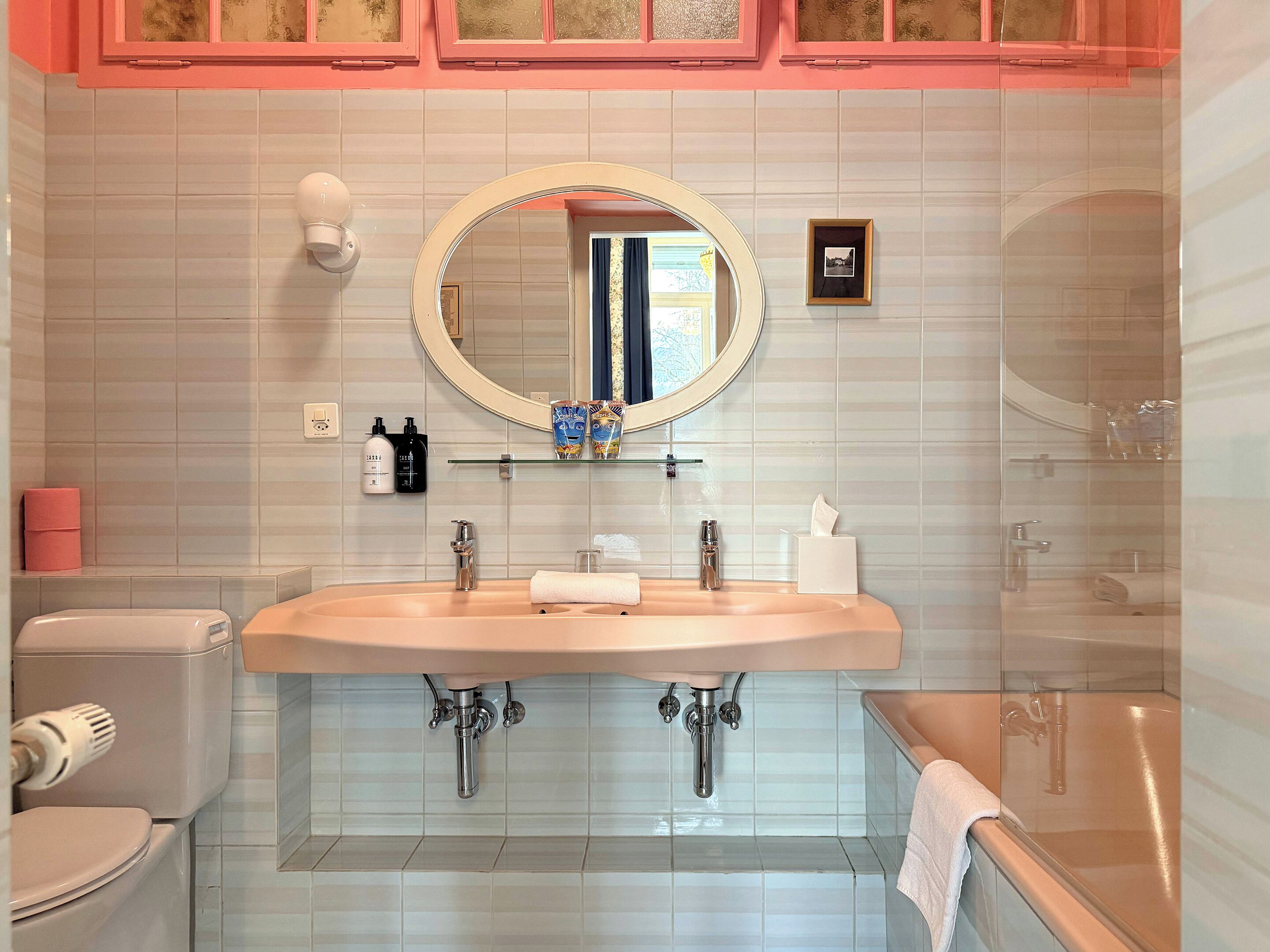 A bathroom with a double sink, a toilet, a shower, and a mirror above the sink.