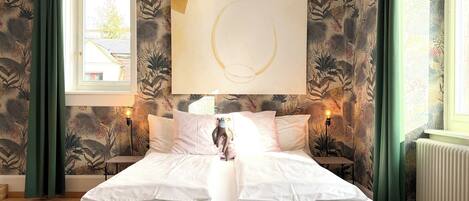 A bedroom with a bed, a wall-mounted abstract painting, and a window with curtains.