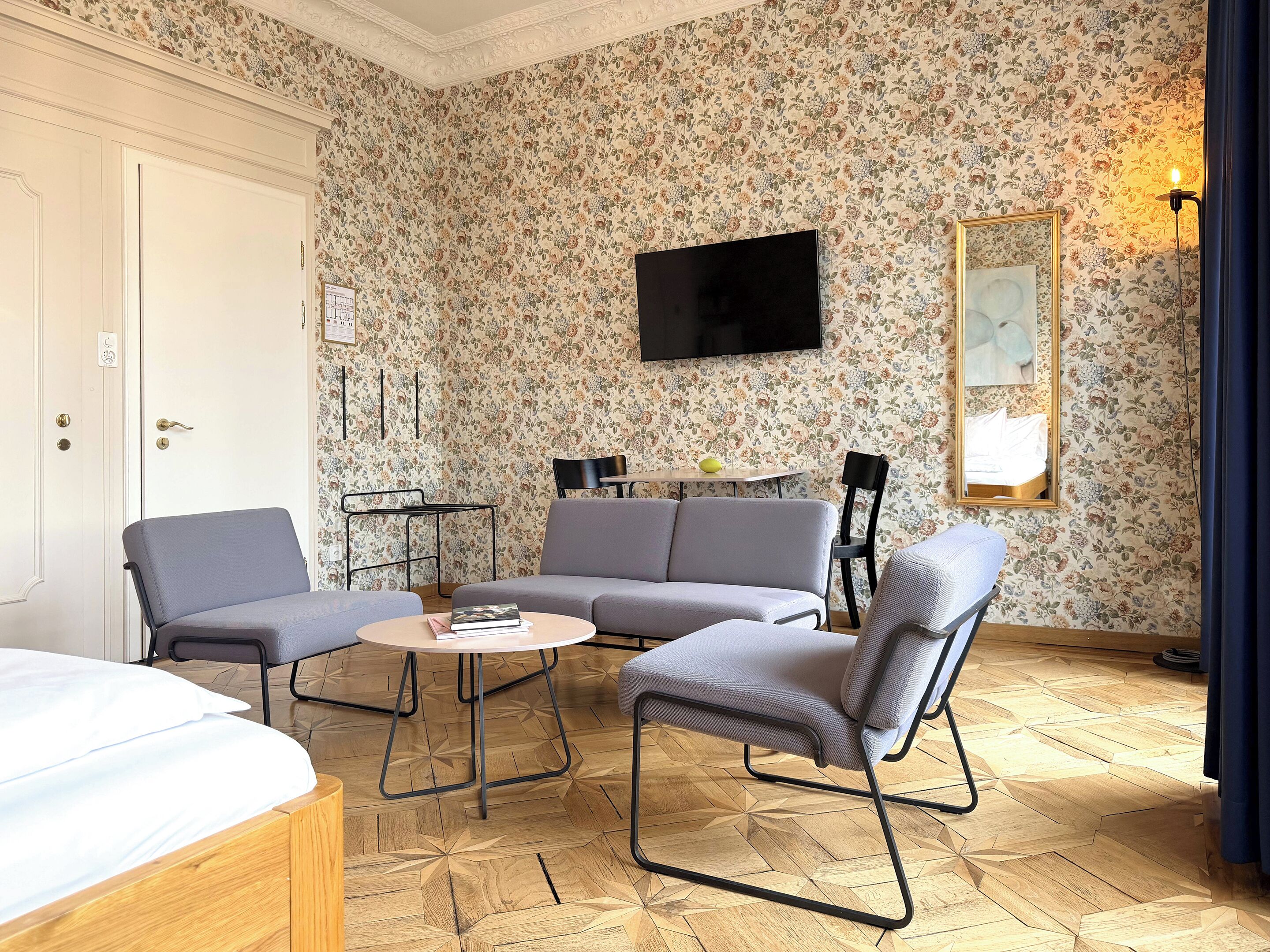 Una habitación de hotel con sofá, dos sillones, una mesita, televisor y cama.
