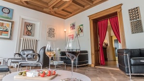 Una sala de estar con techo de madera, sofás de cuero negro, una mesa blanca con una copa de vino y varias obras de arte enmarcadas en las paredes.