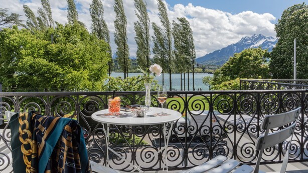 Un balcón con una mesa lista para dos personas, con vista a un lago y montañas.