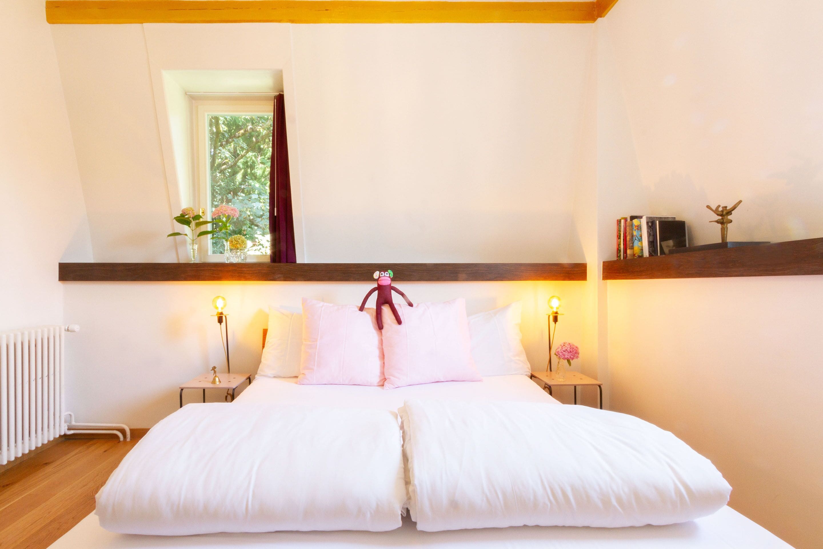 A neatly made bed with white linens, two bedside tables with lamps, and a shelf with books and a decorative item.