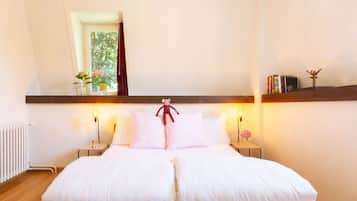 A neatly made bed with white linens, two bedside tables with lamps, and a shelf with books and a decorative item.