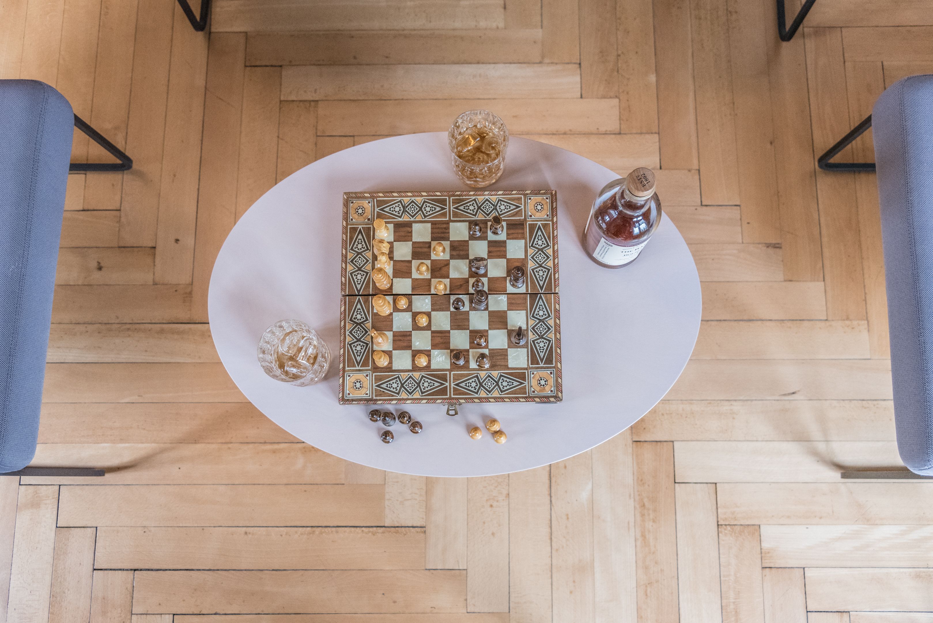 A chessboard on a round table with a bottle and a glass of water beside it.