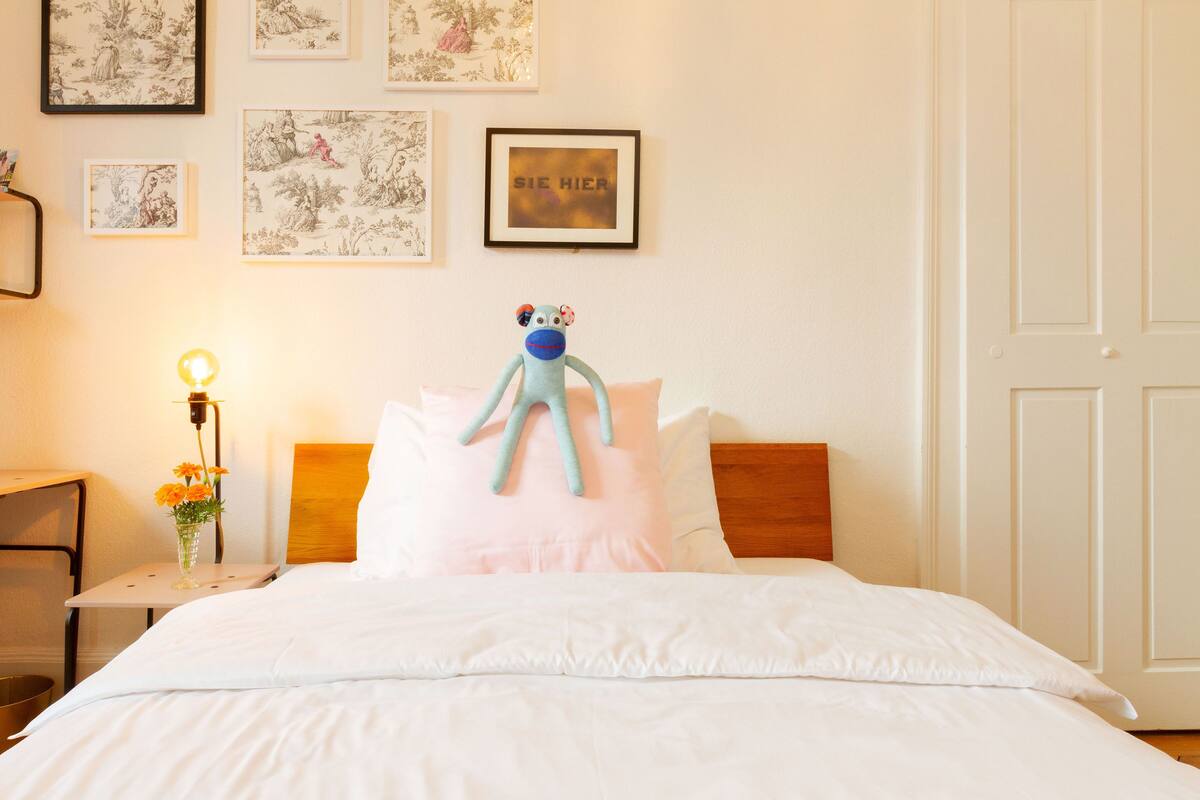Ein Hotelzimmer mit einem Bett, einem Nachttisch mit Lampe und gerahmten Bildern an der Wand.