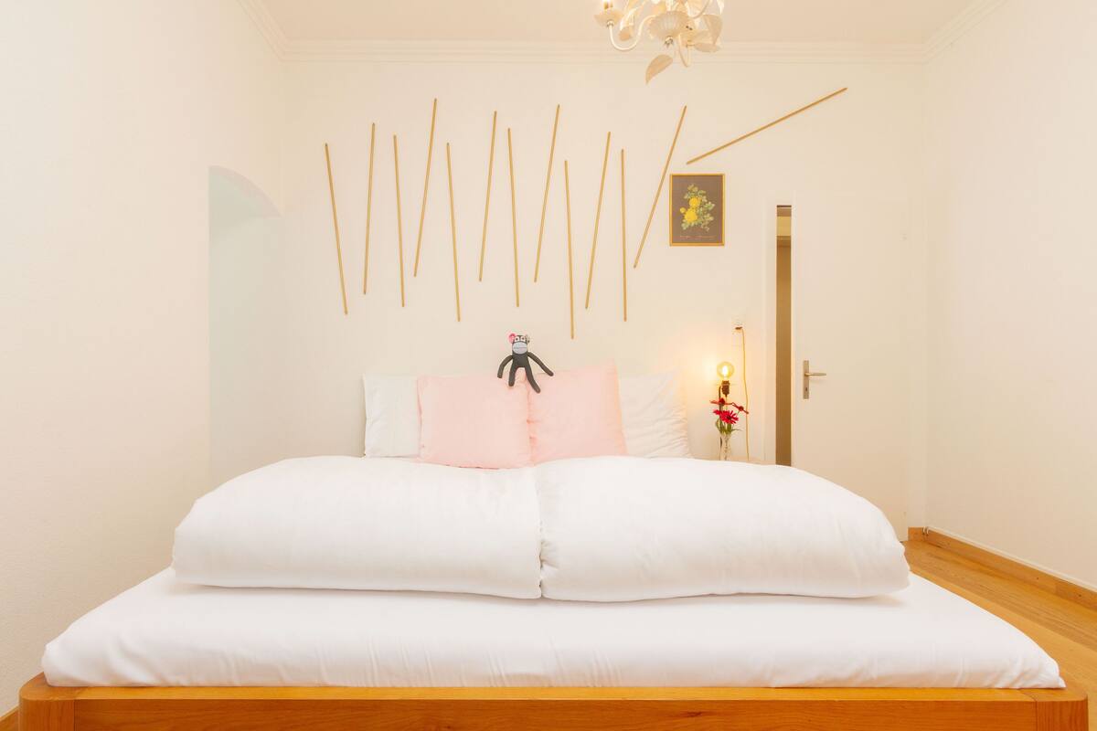 Ein ordentlich bezogenes Bett mit weißer Bettwäsche, einem Holz-Kopfteil und einer Wand mit vertikalen Holzleisten sowie einem kleinen gerahmten Bild.