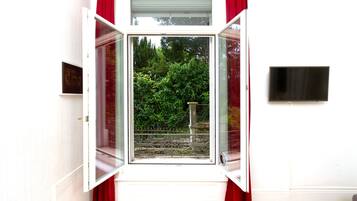 A room with a large window, red curtains, a flat-screen TV mounted on the wall, and a wooden floor.