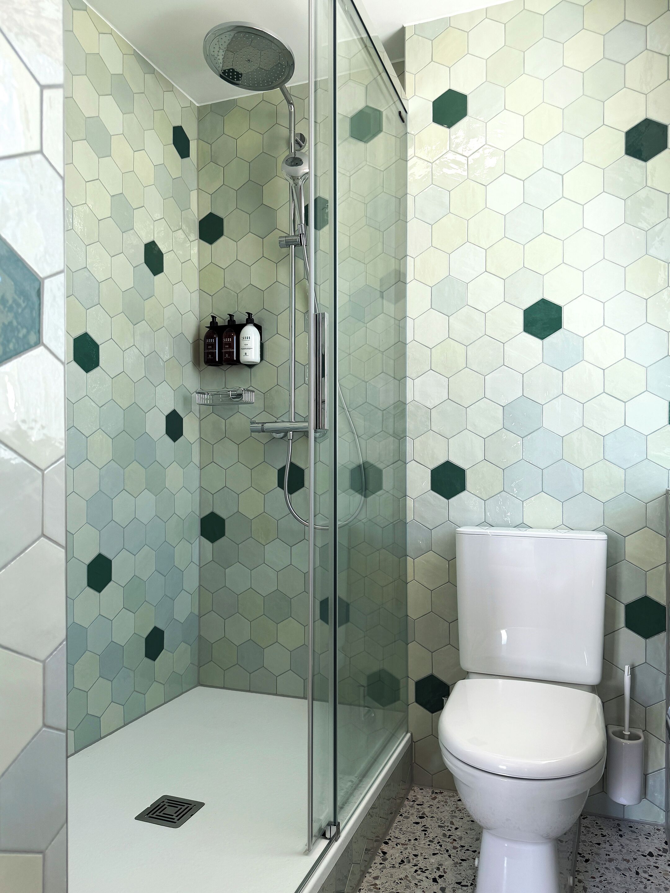 Un baño con ducha de vidrio, inodoro blanco y pared con mosaicos hexagonales.