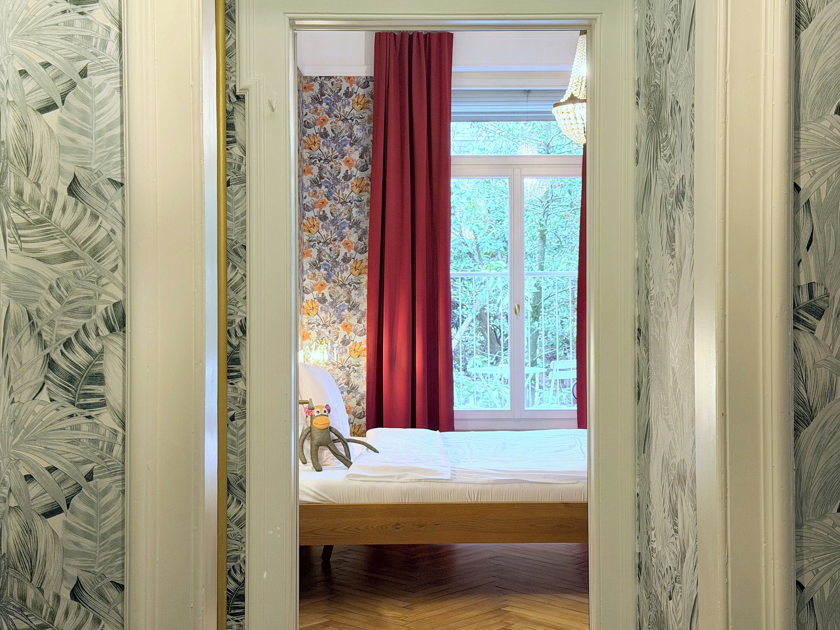 Un dormitorio con una cama, una ventana con cortinas rojas y vistas a zonas verdes.