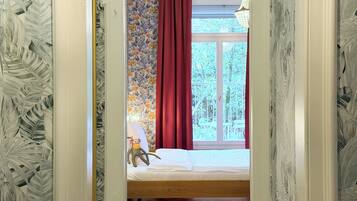 Un dormitorio con una cama, una ventana con cortinas rojas y vistas a zonas verdes.