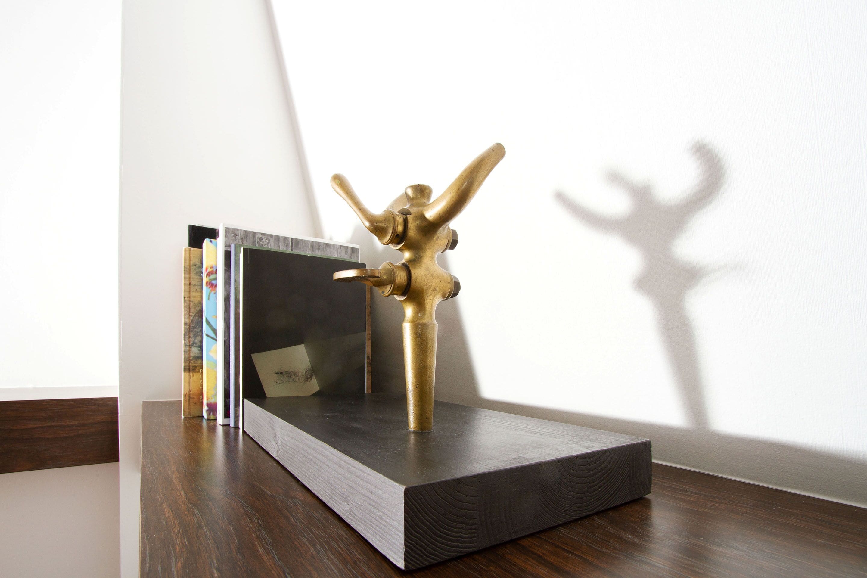 A brass sculpture on a dark wooden platform with books and a framed picture behind it.