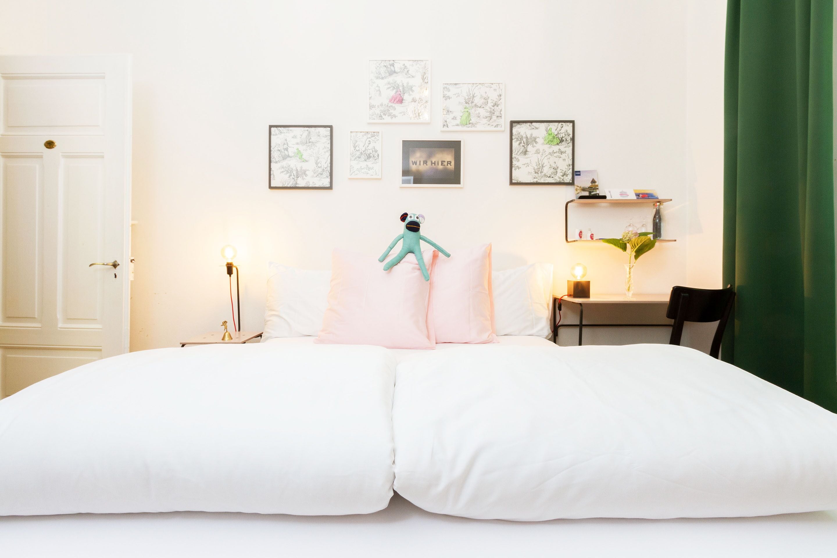 A bedroom with a large bed, a green curtain, and wall art.