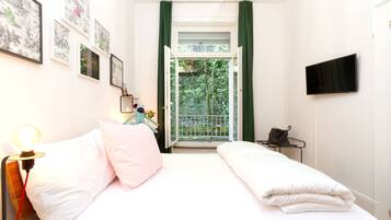 A bedroom with a bed, a bedside table, a lamp, a TV, and a window with green curtains.