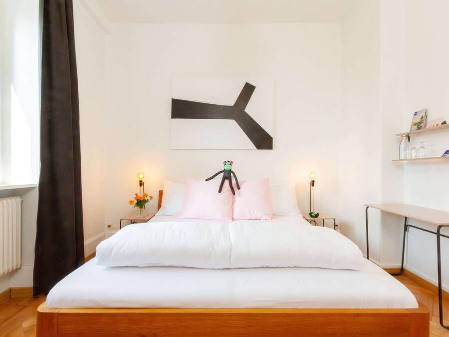 Una cama bien hecha con estructura de madera, un cuadro abstracto en la pared y mesitas de noche con lámparas.
