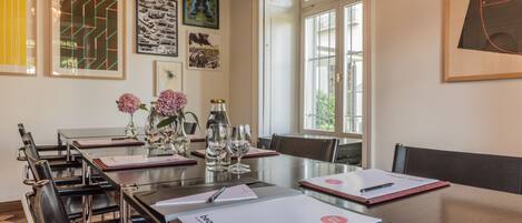 A conference room with a long table, chairs, and various items like a vase with flowers, wine glasses, and documents.