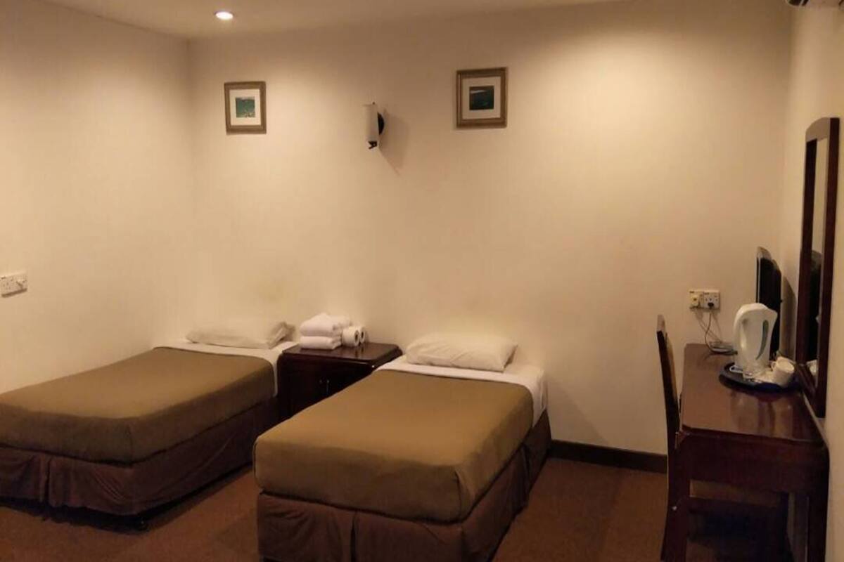 A hotel room with two single beds, a small desk with a chair, and a mirror.