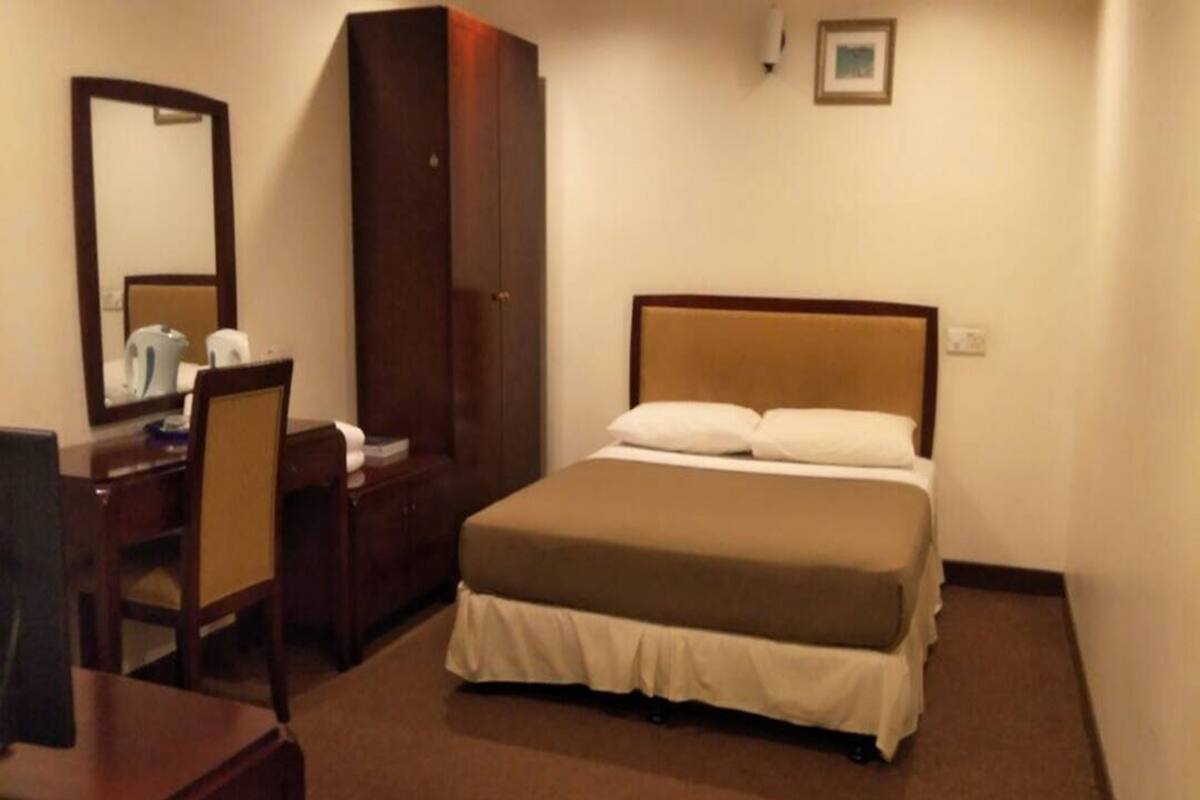 A hotel room with a bed, a desk, a chair, a wardrobe, and a mirror.