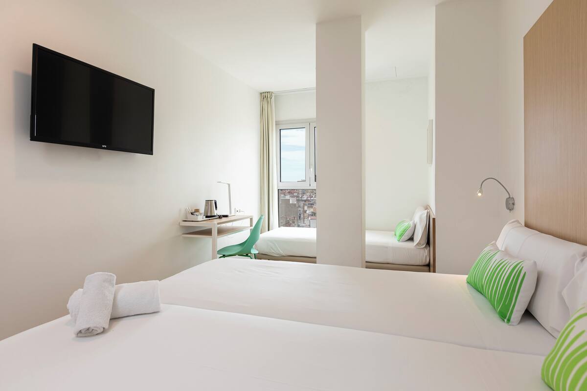 Camera d'albergo con un letto, una scrivania, una sedia, una TV a schermo piatto e vista sulla città dalla finestra.