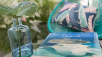 Una botella de vidrio transparente con una planta, un libro titulado 'paraisos' y un adorno con diseño azul y blanco.