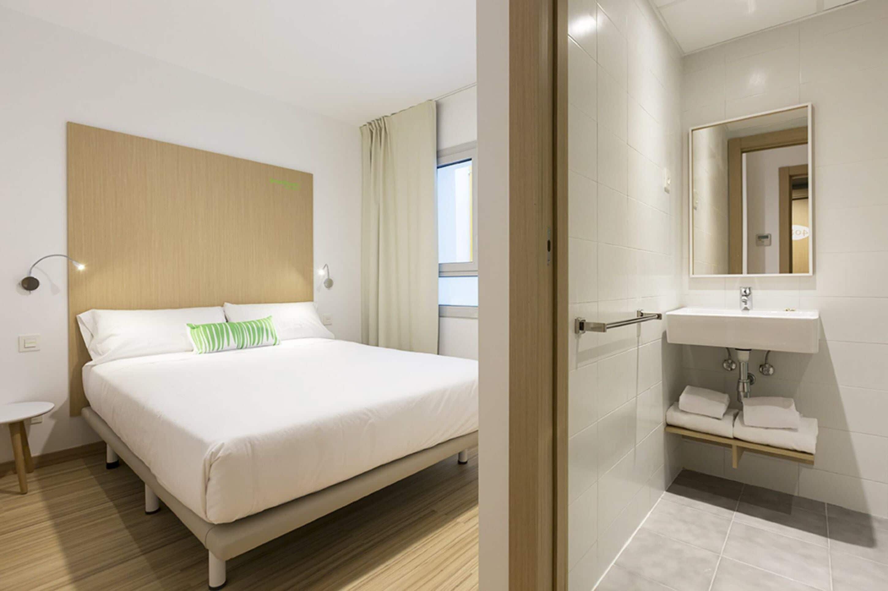 A hotel room with a bed, bedside table, and a bathroom with a sink and mirror.