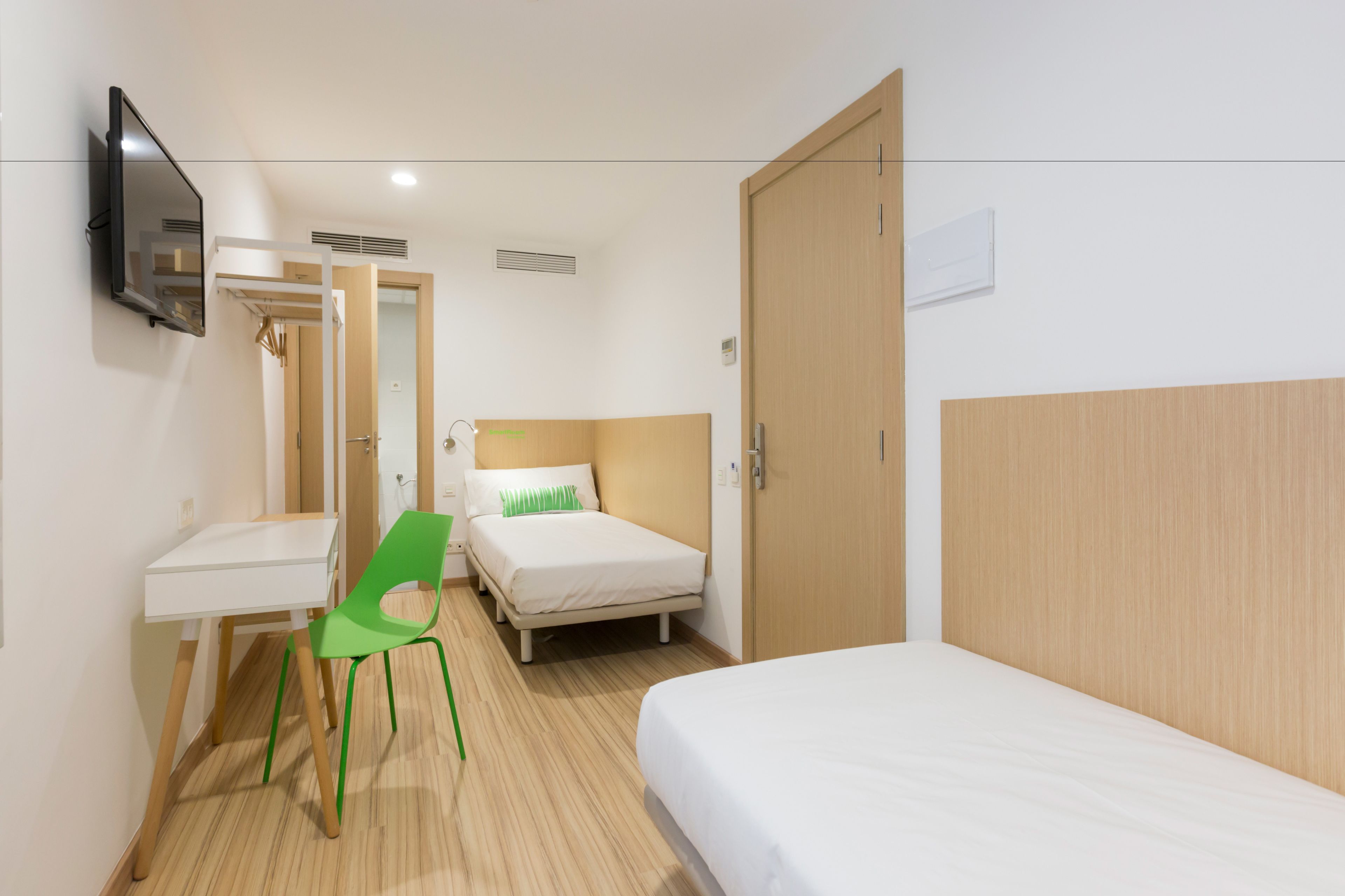 A hotel room with a bed, a desk, a chair, a television, and a door.