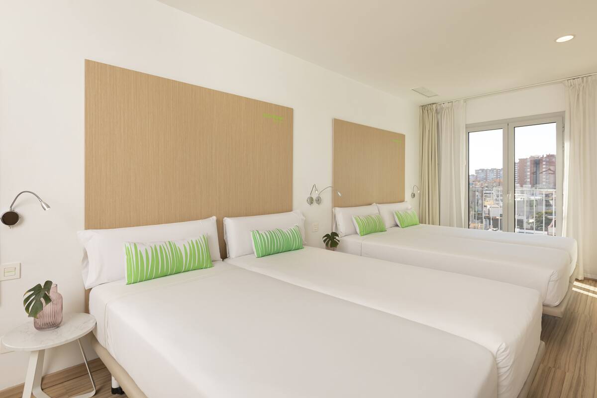 Camera d'albergo con due letti, un tavolino e un'ampia finestra vista città.