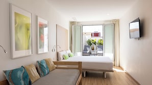 Una habitación de hotel moderna con cama, sofá, televisión y ventanas amplias con vistas a la ciudad.